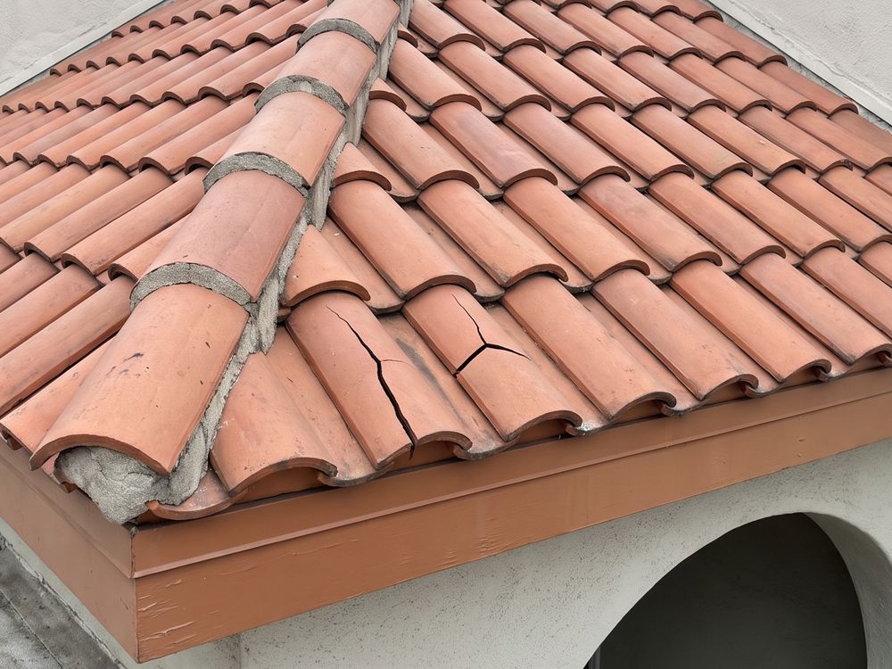 A small clay tile hip roof over an arched apartment entry, every tile in place, with two barrel tiles near the lower edge cracked across